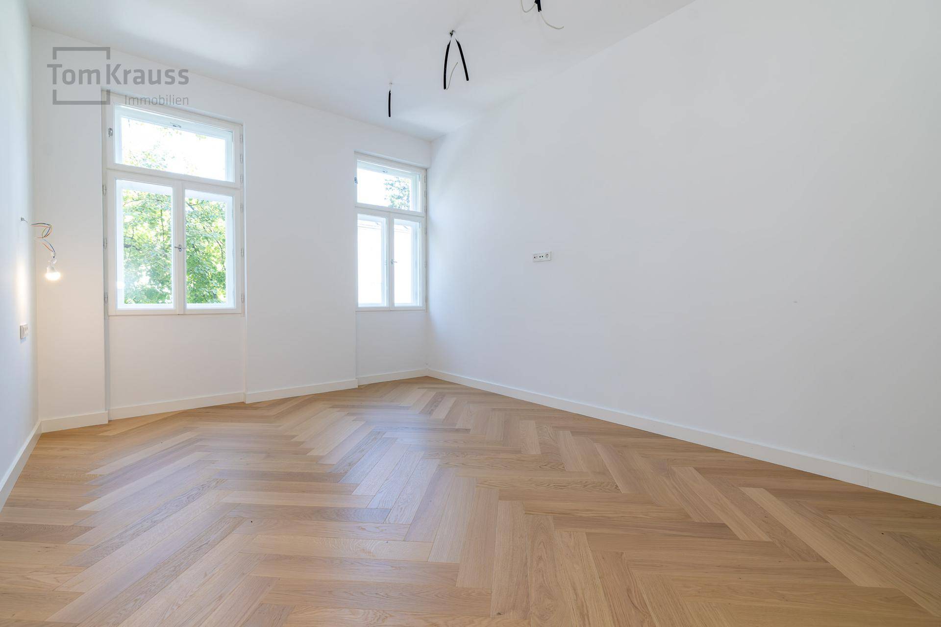 Heller, leerer Raum mit Fischgrätparkett und zwei Fenstern, vielseitig nutzbar.