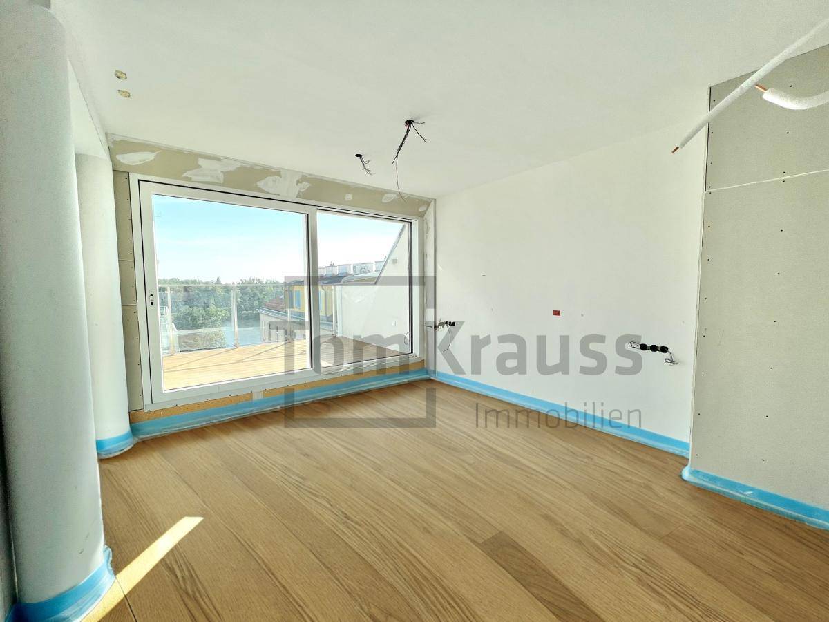 Helles Schlafzimmer im Rohbau mit großem Fenster und neuem Holzboden, bereit für den Ausbau.