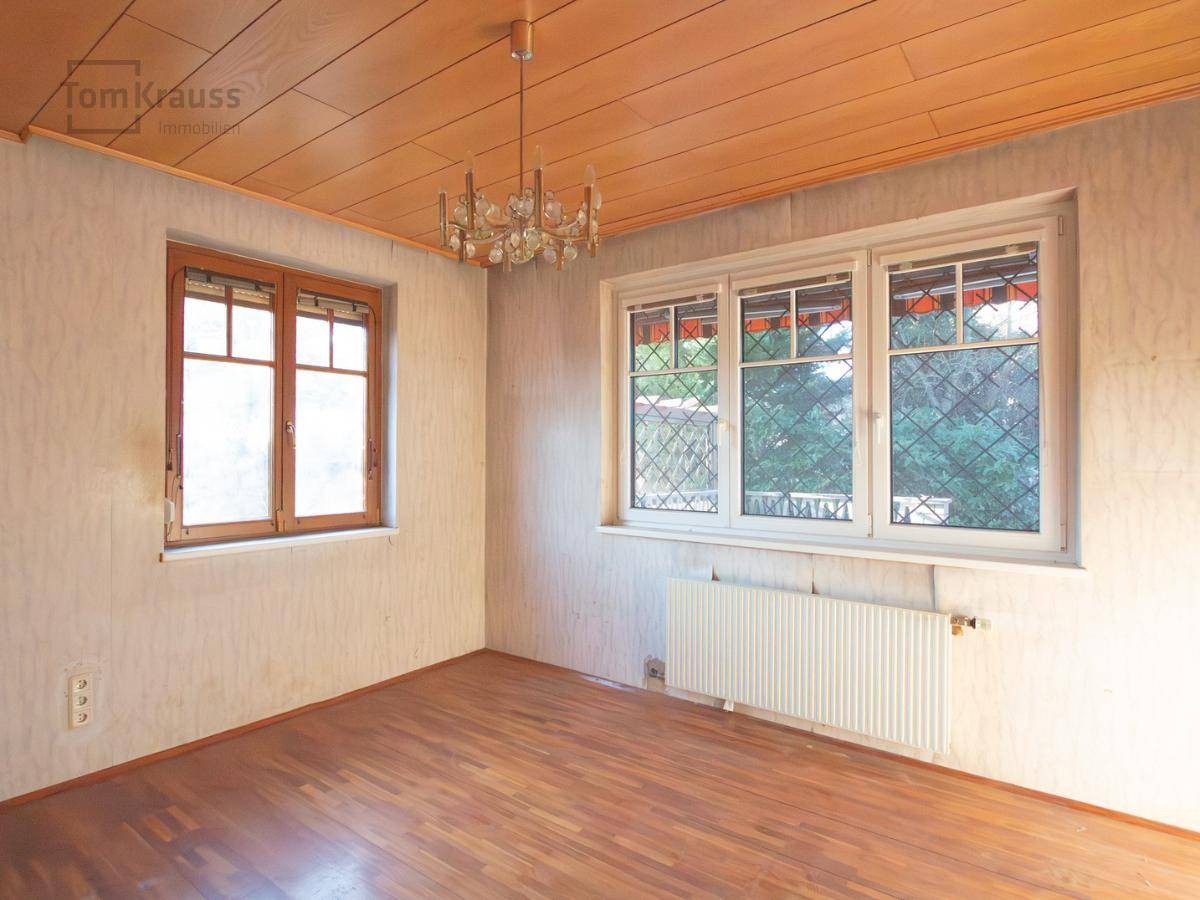 Leeres Zimmer mit Parkettboden, Holzdecke und zwei Fenstern, bereit für eine Renovierung.