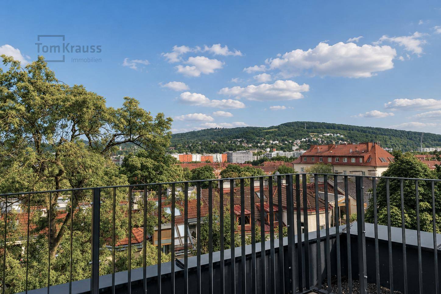 Panoramablick von einer Dachterrasse über die Stadt und die bewaldeten Hügel im Hintergrund.