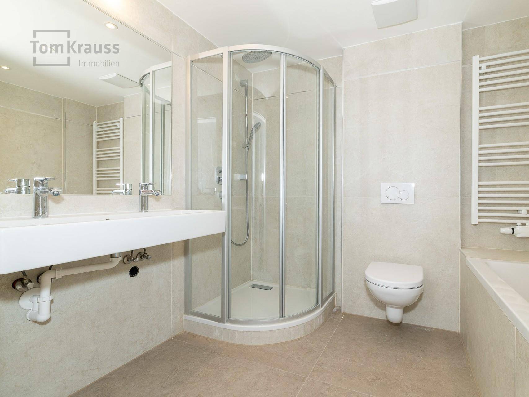 Helles Badezimmer mit Duschkabine, Doppelwaschbecken und modernen Fliesen.