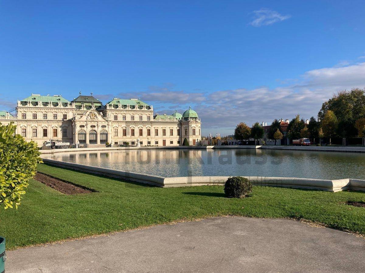 Prächtiges Schloss mit großem Teich und weitläufiger Gartenanlage unter blauem Himmel.