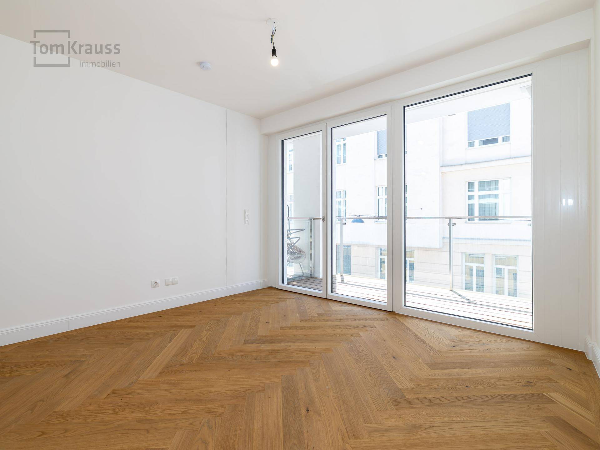 Geräumiges Zimmer mit Fischgrätparkett und großen Fenstern, die viel Tageslicht bieten.