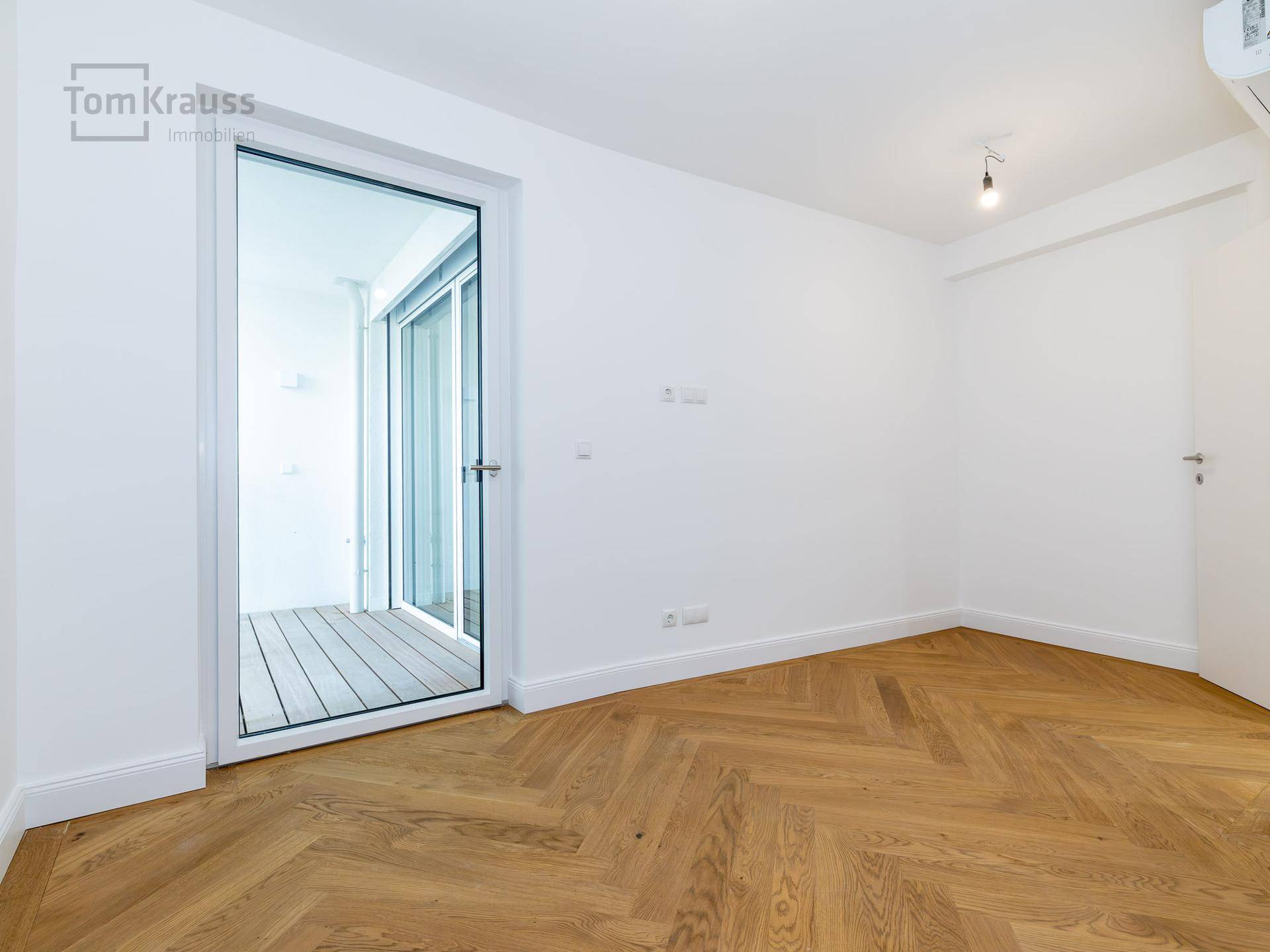 Helles Zimmer mit Fischgrätparkett und direktem Zugang zu einem Balkon.
