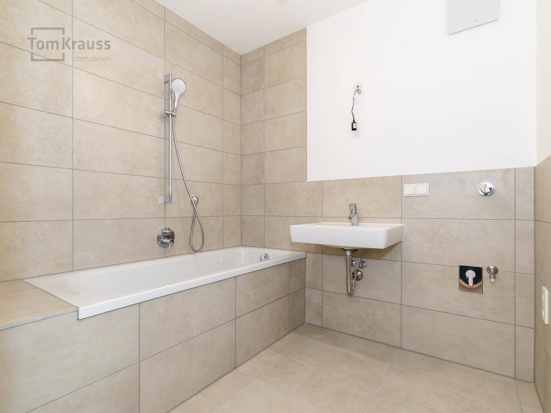 Unmöbliertes Badezimmer mit Badewanne und Waschbecken, bereit für die Installation eines Spiegels.