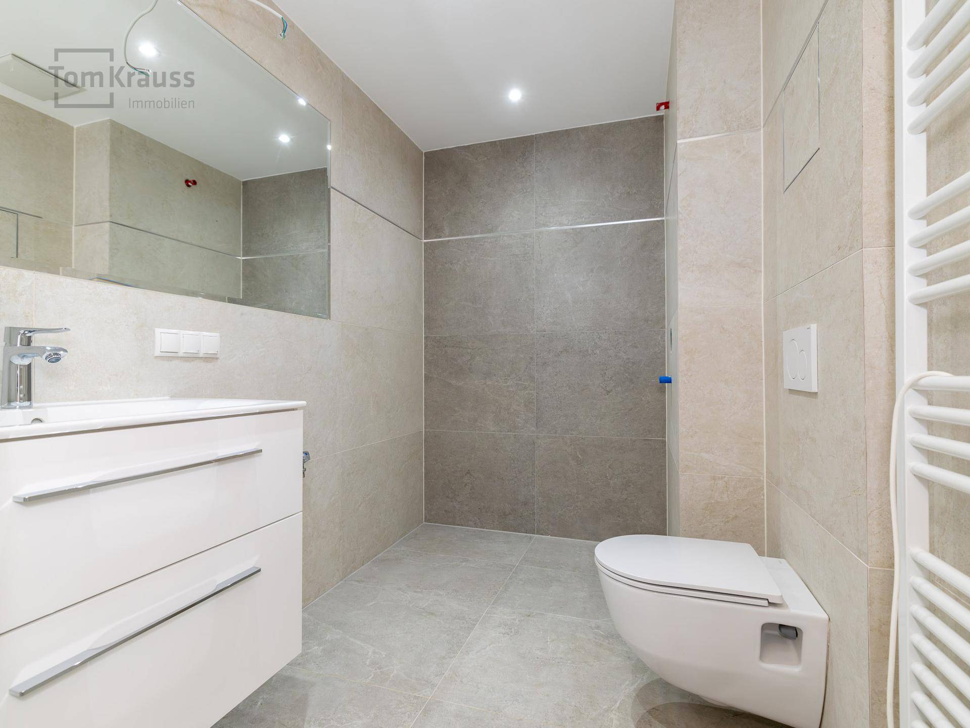 Helles Badezimmer mit beigefarbenen Fliesen, Wand-WC und Waschtischunterschrank, bereit für die Dusche.