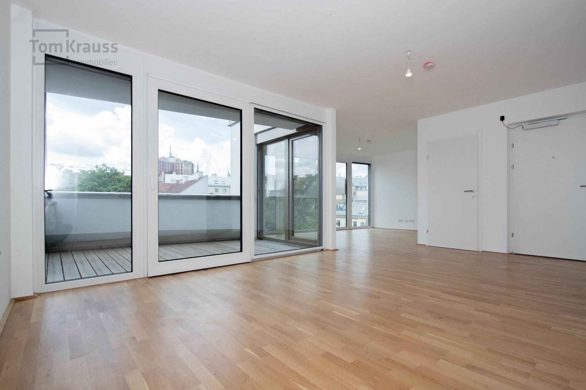 Geräumiger, heller Raum mit Holzboden und großen Schiebetüren zum Balkon.