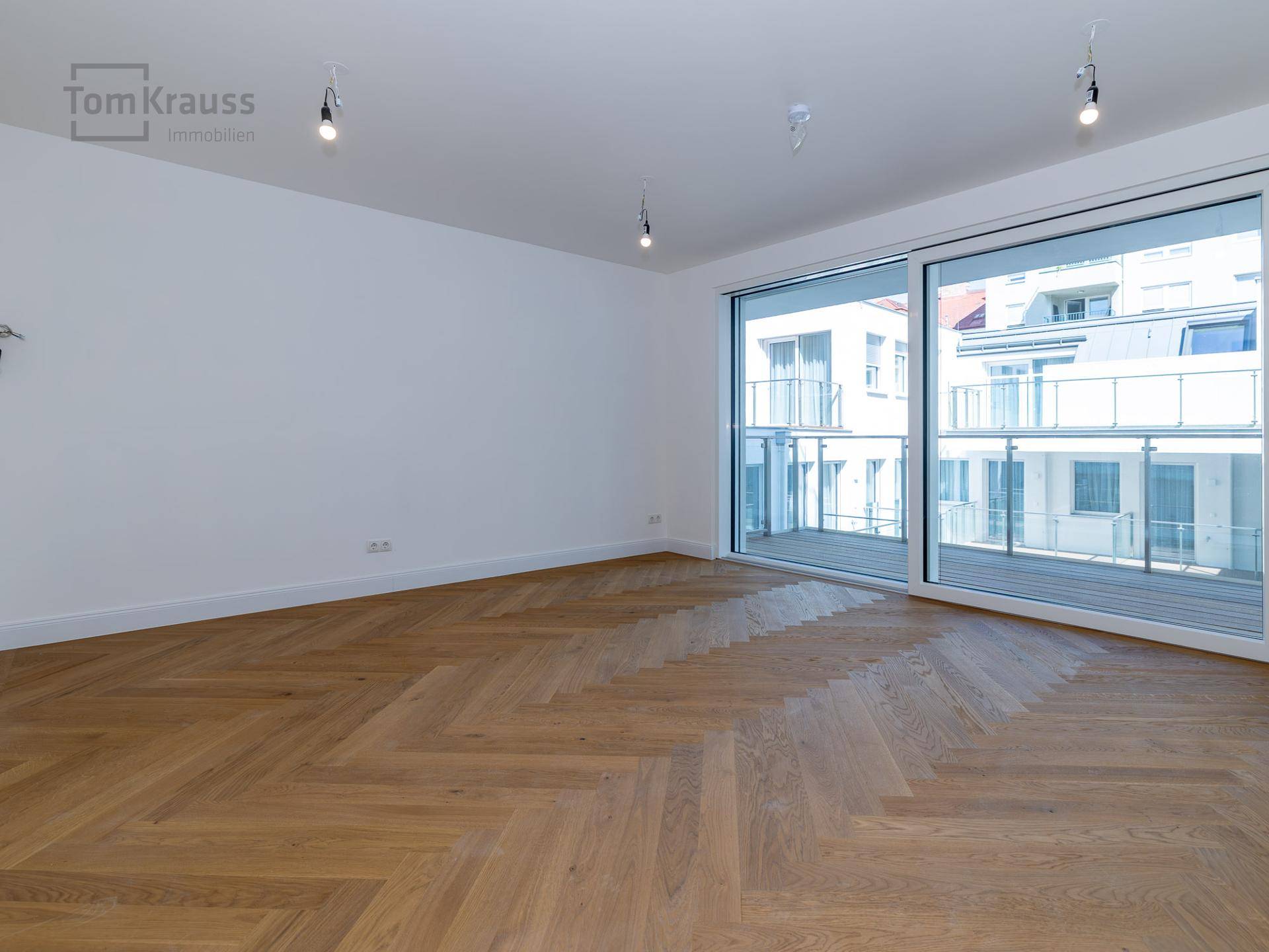 Heller und geräumiger Raum mit Fischgrätparkett und großen Fenstern zum Balkon.