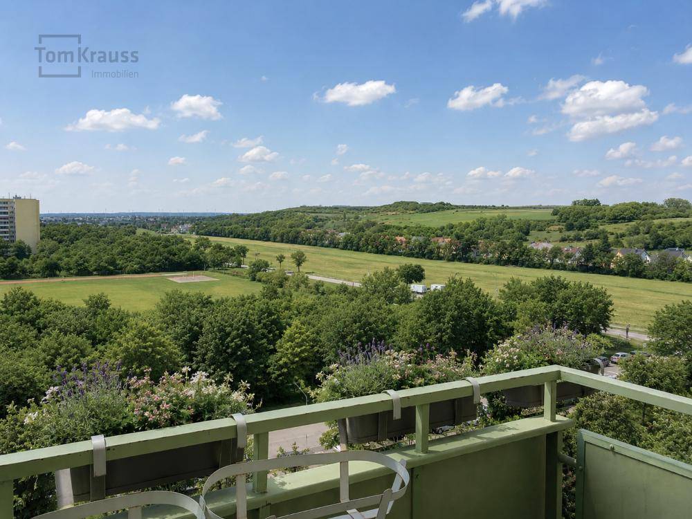 Blick vom Balkon auf weite grüne Felder und bewaldete Hügel unter blauem Himmel.