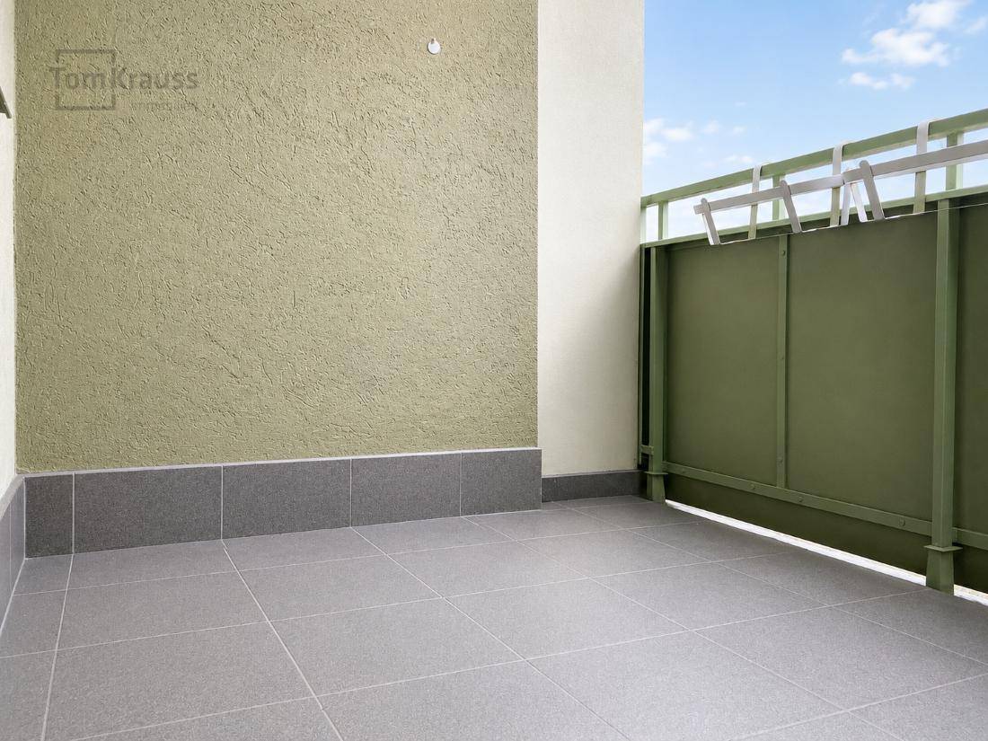 Geräumiger Balkon mit Fliesenboden und grüner Wand, bereit zur Gestaltung.