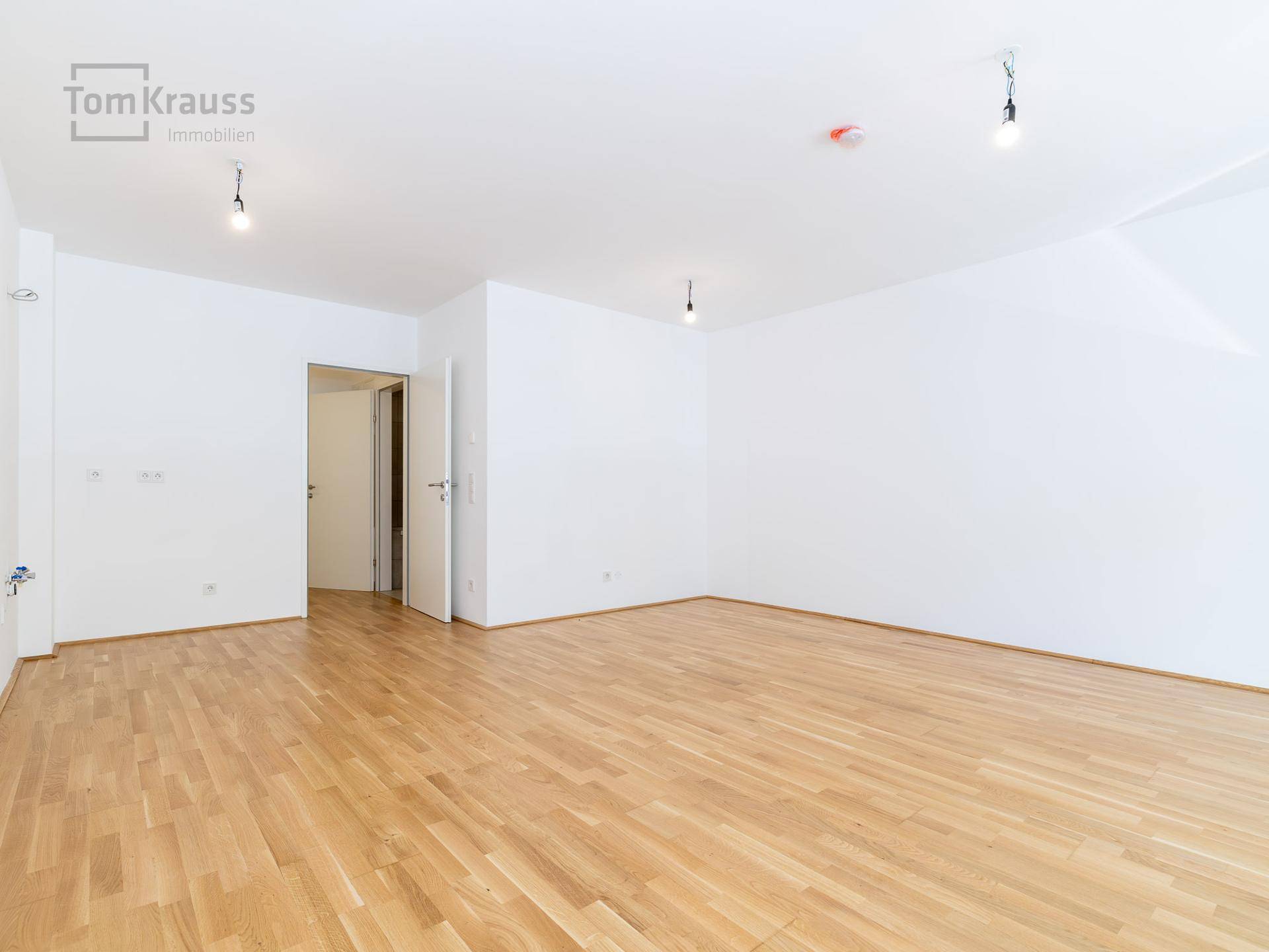 Helles, leeres Zimmer mit Parkettboden und Zugang zu weiteren Räumen, ideal zur individuellen Gestaltung.