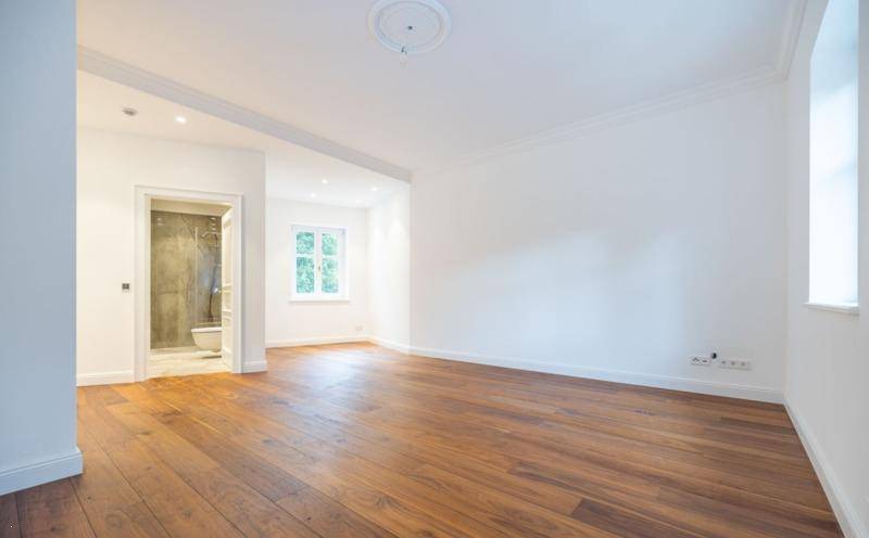 Helles Zimmer mit Holzboden und Zugang zu einem modernen Badezimmer, ideal als Schlaf- oder Wohnbereich.
