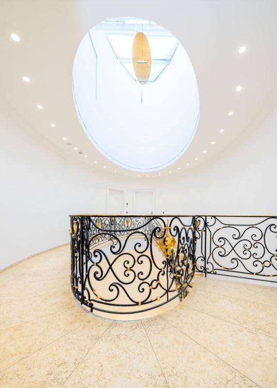 Oberer Bereich der Treppe mit kunstvollem Geländer und einem ovalen Oberlicht, das den Raum erhellt.