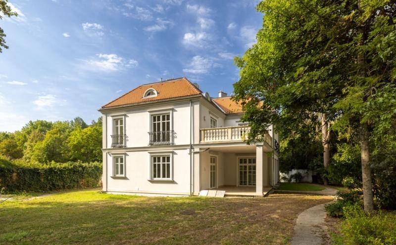 Elegante Villa von der Gartenseite, umgeben von altem Baumbestand und weitläufigen Grünflächen.
