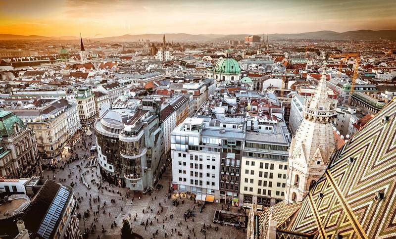 Luftaufnahme einer belebten Stadt mit vielen Gebäuden und einer Kathedrale bei Sonnenuntergang.