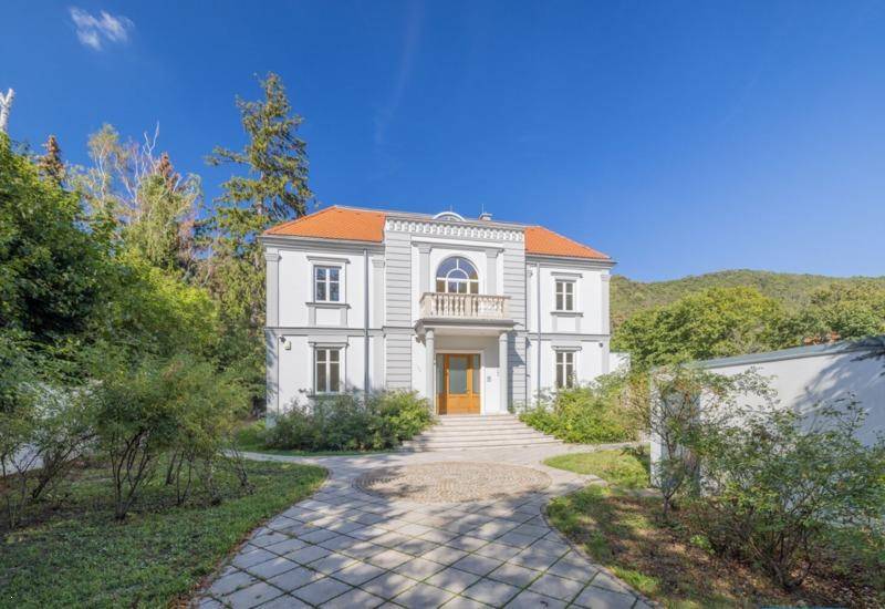 Prächtige Villa mit gepflasterter Auffahrt und umgebender Natur unter blauem Himmel.