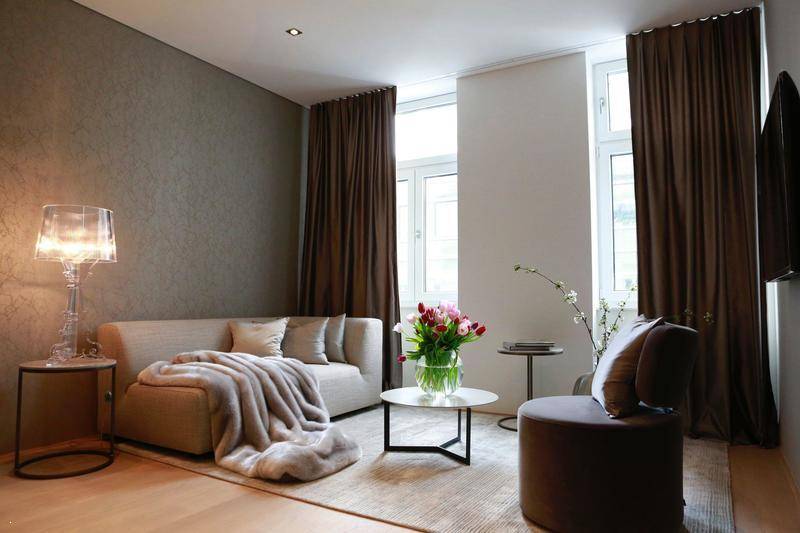 Elegantes Wohnzimmer mit beigem Sofa, Stehlampe und hohen Fenstern mit braunen Vorhängen.