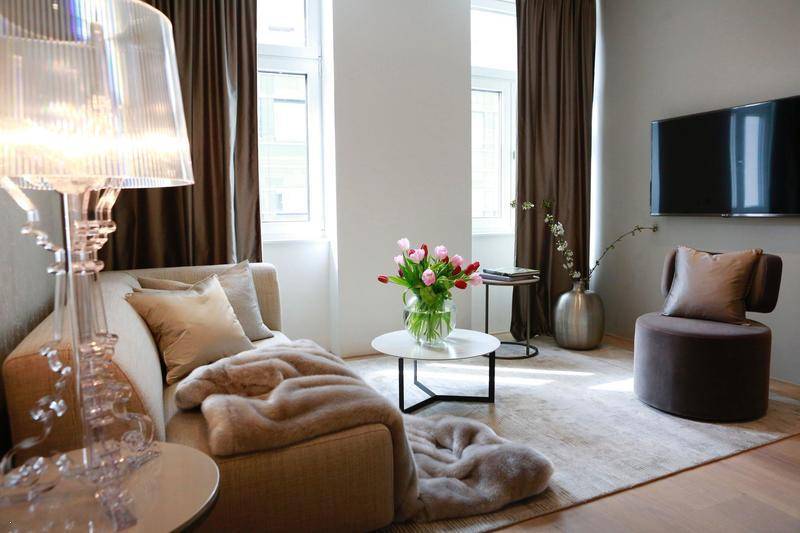 Modernes Wohnzimmer mit Wandfernseher, beigem Sofa und großen Fenstern für viel Licht.