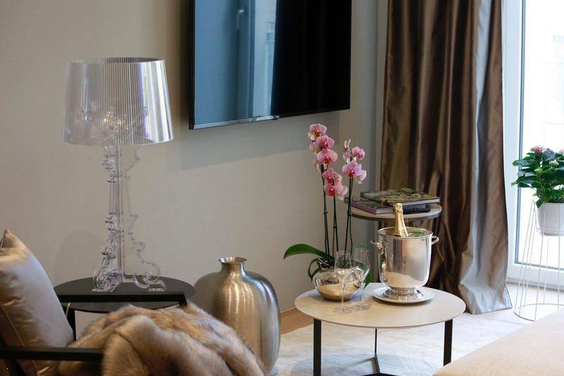 Gemütlicher Wohnbereich mit Wandfernseher, Couch und dekorativen Elementen wie einer Orchidee und Champagner.