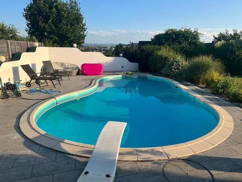 Sonniger Poolbereich mit Sprungbrett, Liegestühlen und einer ummauerten Terrasse im Grünen.