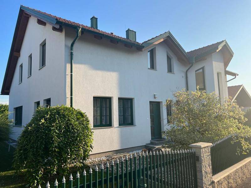 Ansicht des Hauses von der Seite mit grünen Fensterrahmen und üppiger Bepflanzung im Vorgarten.