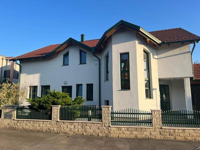Gepflegtes Einfamilienhaus mit weißer Fassade, grünen Fensterrahmen und dekorativer Steinmauer.