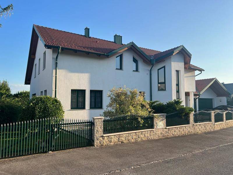 Gesamtansicht des Hauses mit weißer Fassade, rotem Dach und umzäuntem Vorgartenbereich.