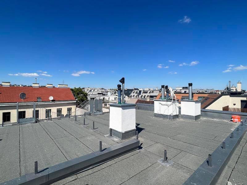 Blick über die Dächer der Stadt mit Schornsteinen und Lüftungsanlagen unter klarem Himmel.