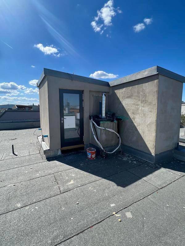 Ein kleiner Aufbau auf einem Flachdach mit einer Tür und sichtbaren Installationen.