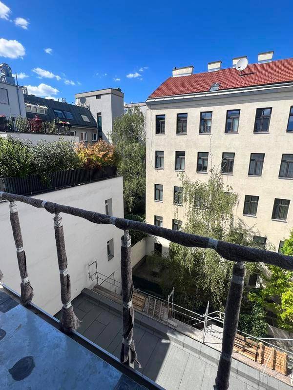 Blick von einem Balkon in einen begrünten Innenhof mit Bäumen und umliegenden Gebäuden.