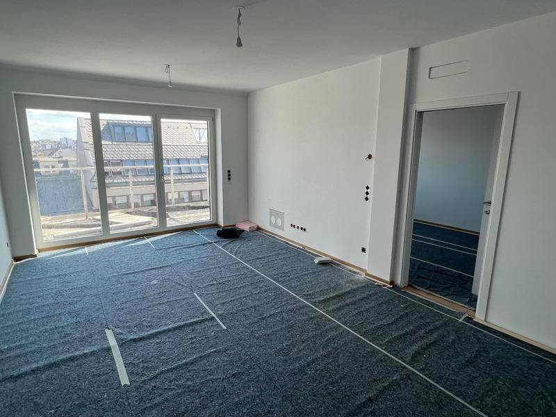 Helles Wohnzimmer mit großen Fenstern und Blick auf die Dächer, Boden ist für Verlegung vorbereitet.