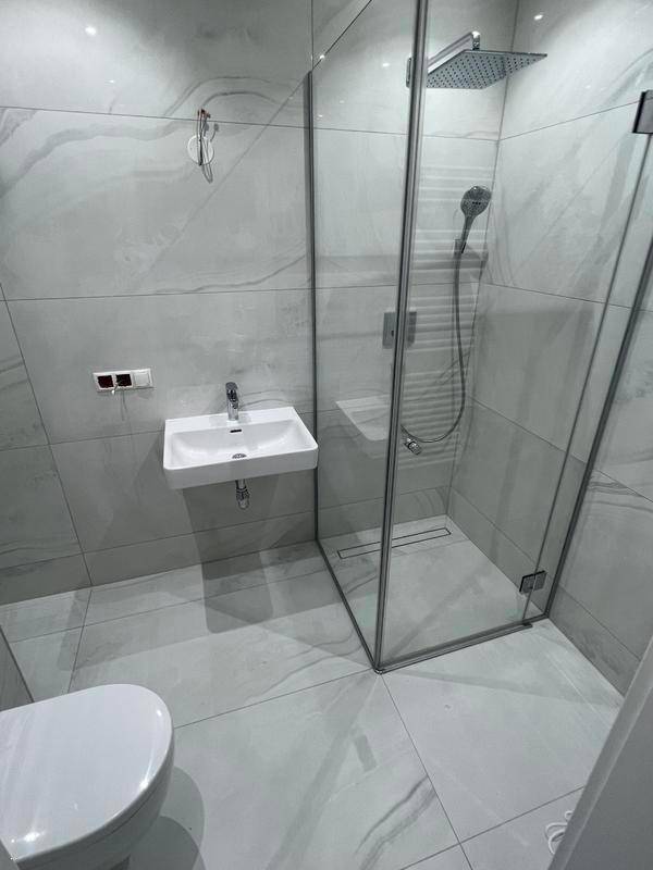 Modernes Badezimmer mit Duschkabine, Waschbecken und Wand-WC in hellgrauen Fliesen.