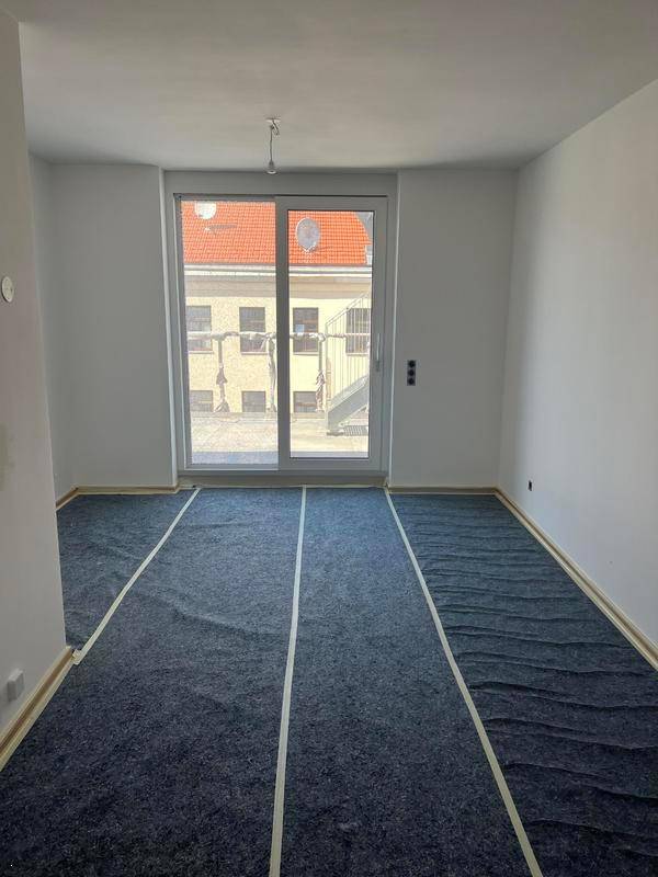 Geräumiges Wohnzimmer mit großen Fenstern und vorbereitetem Boden für die Verlegung.