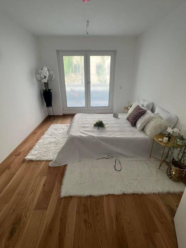 Schlafzimmer mit Holzboden, einem großen Fenster und weißer, minimalistischer Einrichtung.