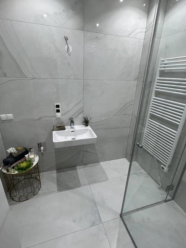 Modernes Badezimmer mit grauen Fliesen, einem Waschbecken und einer Duschkabine.