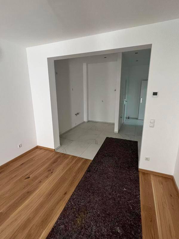 Flur mit Holzboden und einem dunklen Teppich, der den Übergang zu einem gefliesten Bereich markiert.