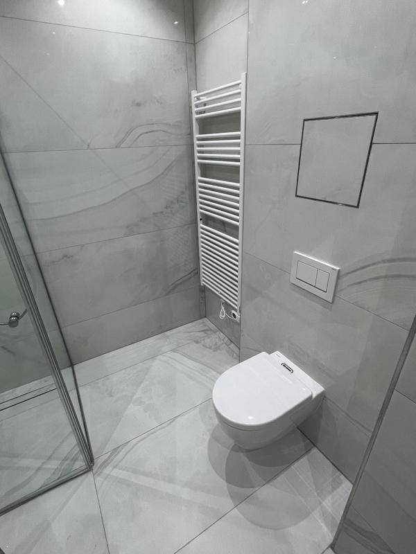 Modernes Badezimmer mit Wand-WC, Handtuchheizkörper und grauen Fliesen.