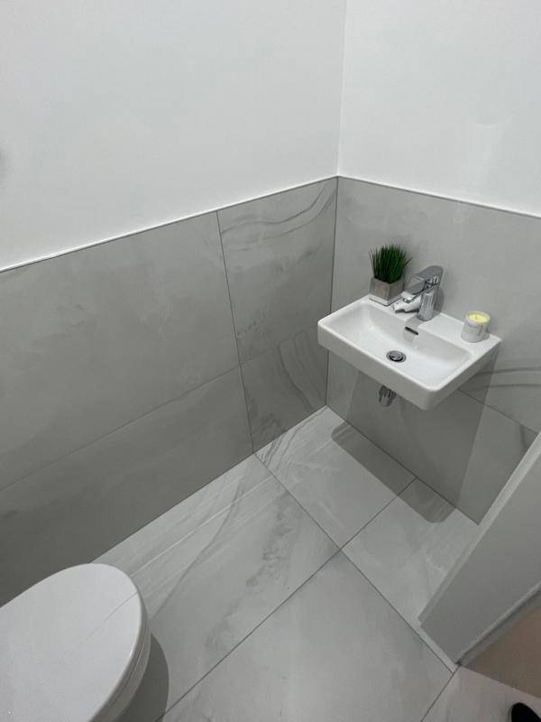 Kleines Gäste-WC mit modernem Waschbecken und halbhohen grauen Fliesen.