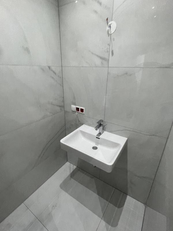 Modernes Badezimmer mit kleinem Waschbecken und grauen Fliesen an Wänden und Boden.