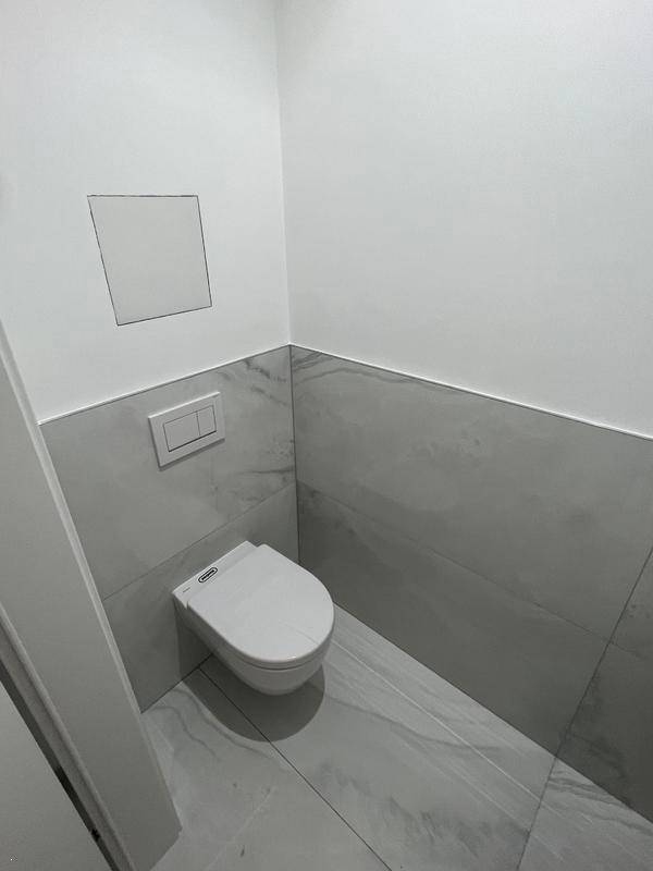 Gäste-WC mit Wand-WC und halbhohen grauen Fliesen, die einen modernen Look verleihen.