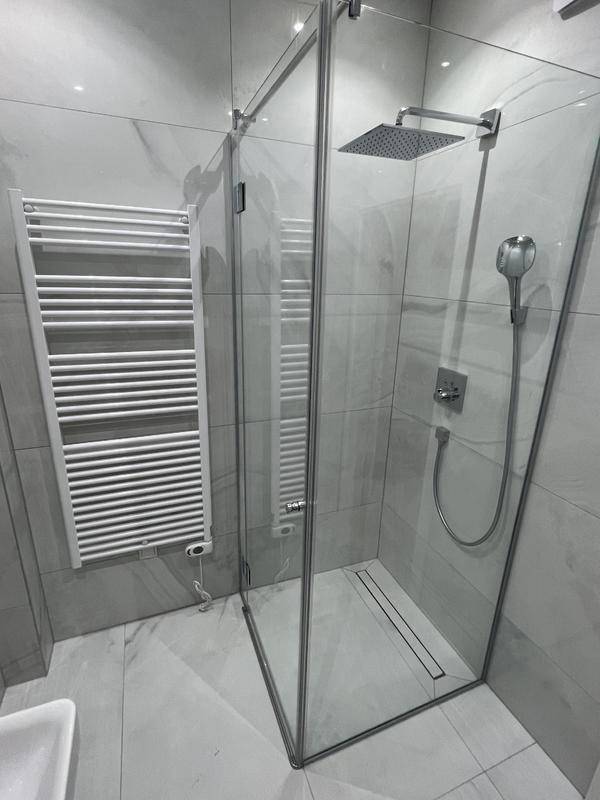 Modernes Badezimmer mit Duschkabine, Handtuchheizkörper und eleganten grauen Fliesen.