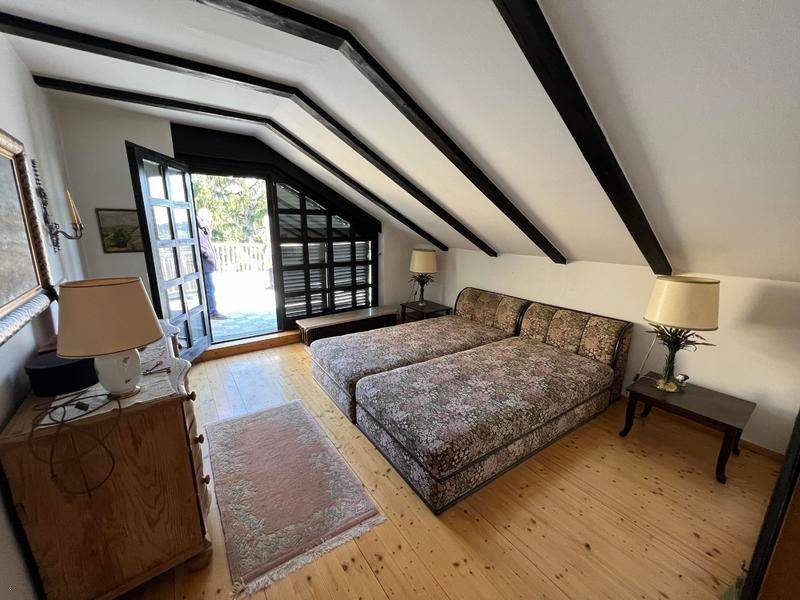 Dachschlafzimmer mit schrägen Decken, Holzbalken und Zugang zu einem Außenbereich.