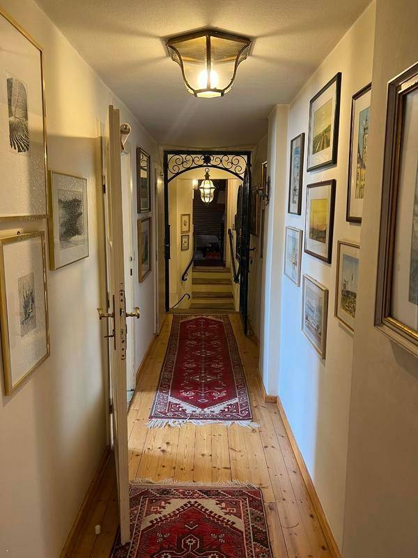 Heller Flur mit Holzplankenboden, roten Teppichen und einer Galerie von Bildern an den Wänden.