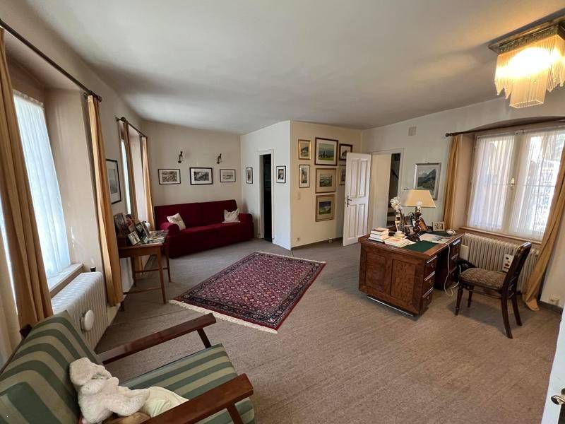Geräumiger Wohnraum mit Teppichboden, rotem Sofa und einem klassischen Schreibtisch, hell und einladend.