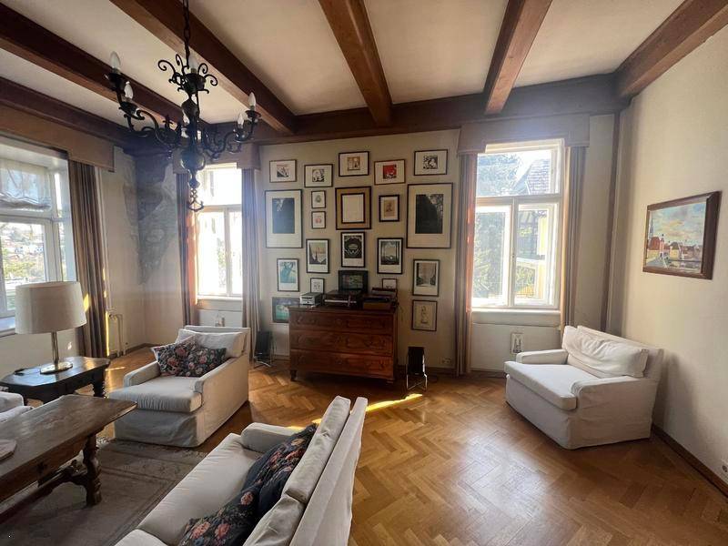 Helles Wohnzimmer mit Holzbalkendecke, Fischgrätparkett und einer Bildergalerie an der Wand.