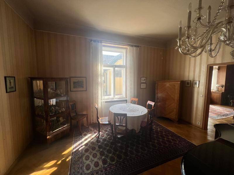 Gemütliches Esszimmer mit gestreifter Tapete, kleinem Esstisch und Kronleuchter, durchflutet von Sonnenlicht.