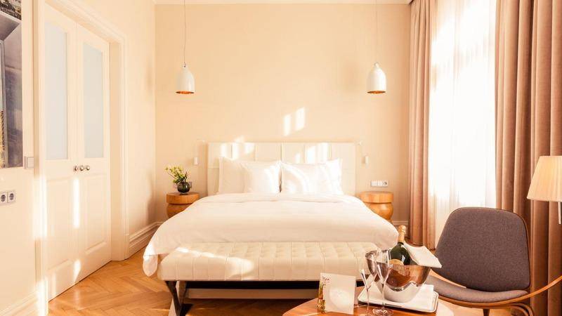 Helles Schlafzimmer mit Parkettboden, großen Fenstern und gemütlicher Sitzecke, sonnendurchflutet.