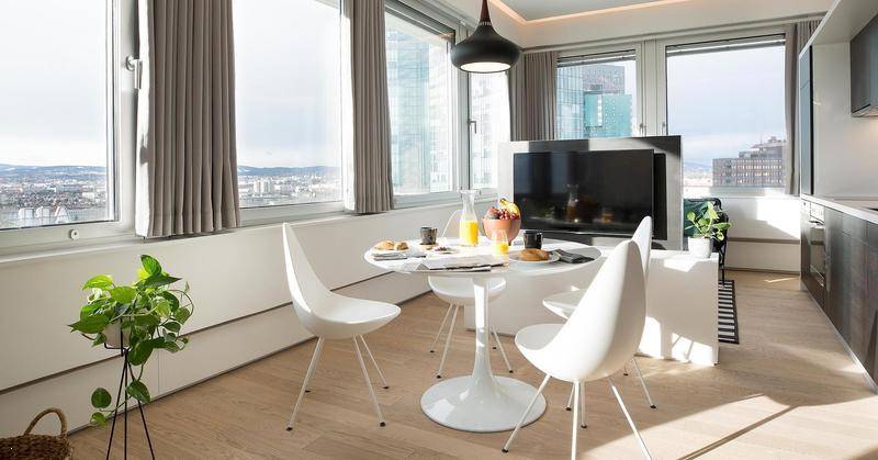 Heller Essbereich mit modernem runden Tisch und Stühlen, umgeben von großen Fenstern mit Stadtblick.