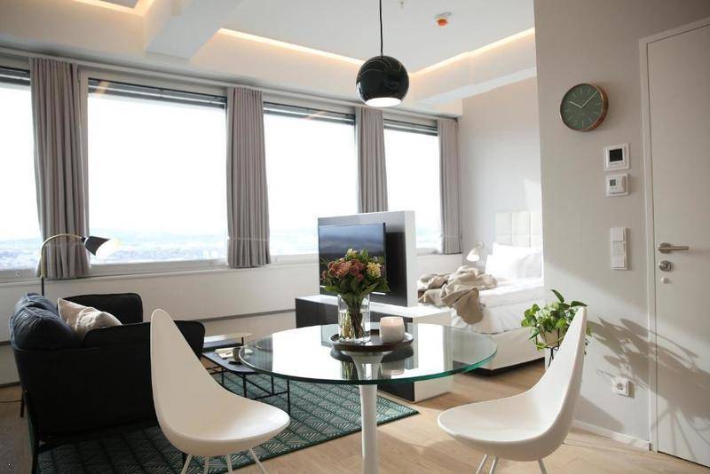 Helles Studio-Apartment mit Schlafbereich, Wohnbereich und Essbereich, umgeben von großen Fenstern.