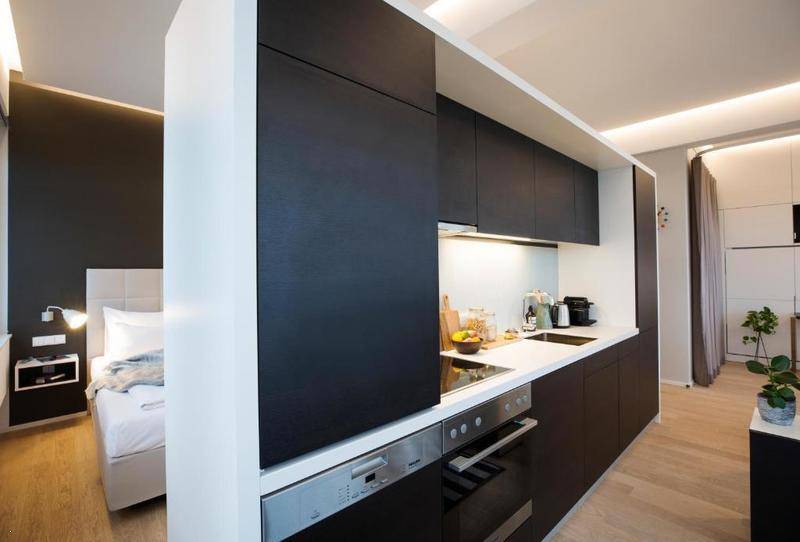 Moderne schwarze Einbauküche mit Spülmaschine und Blick auf den angrenzenden Schlafbereich.